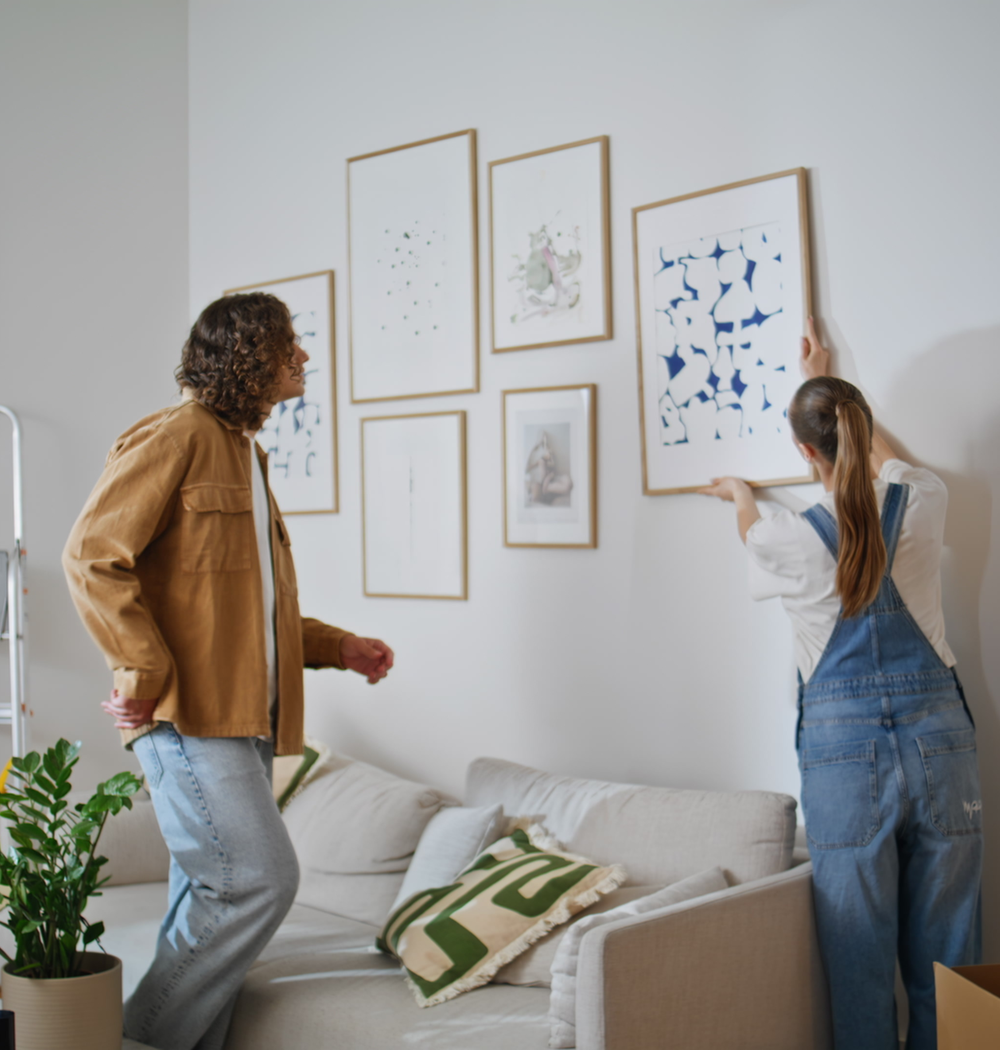 Paar hängt Bilderrahmen in einem fast fertig eingerichteten Zimmer auf