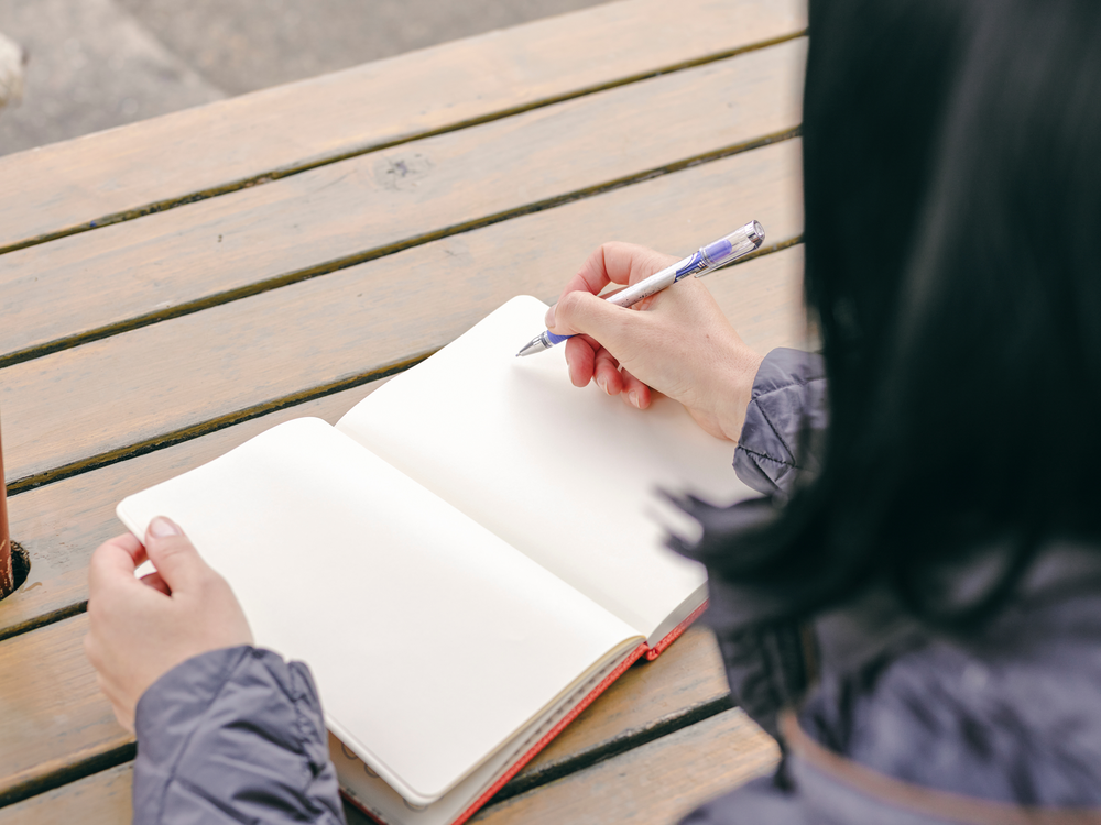 Frau notiert etwas in ein kleines Buch an einem Tisch im Freien