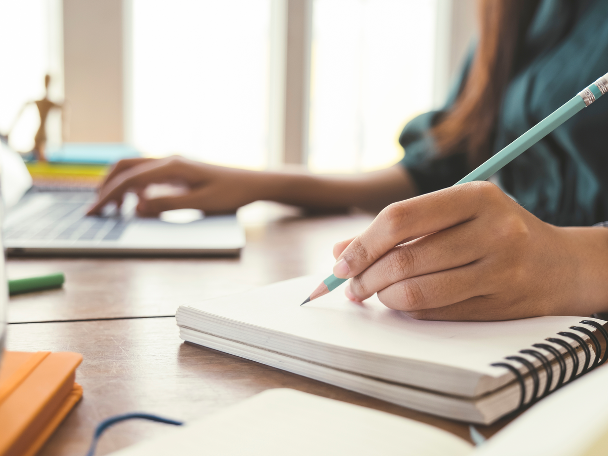 Hände mit Stift und Notizblock an einem hellen Schreibtisch