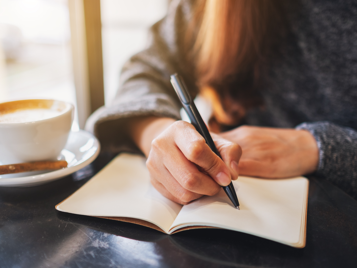 Frau schreibt mit einem Kaffee am Fenster in ein Notizbuch