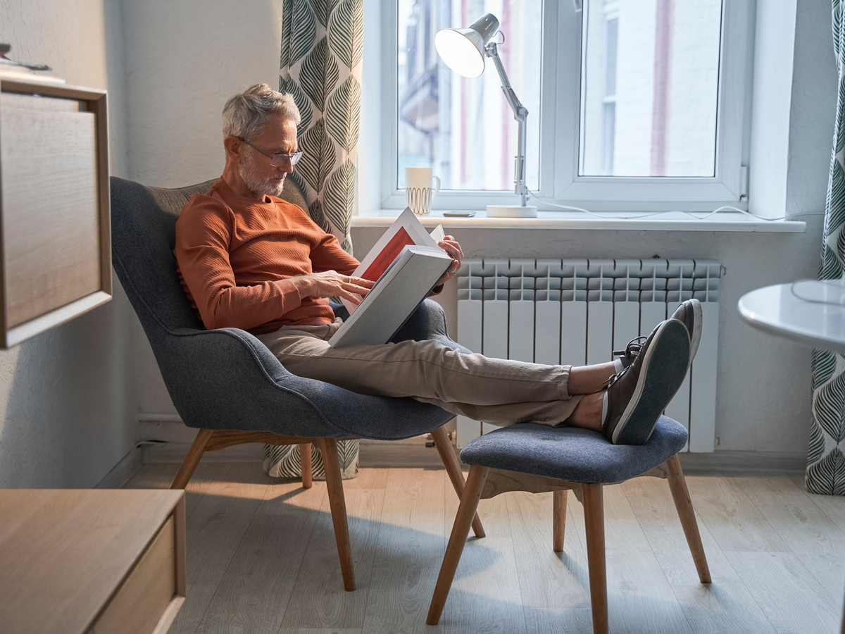 Mann liest in einem Sessel am Fenster in einem Buch