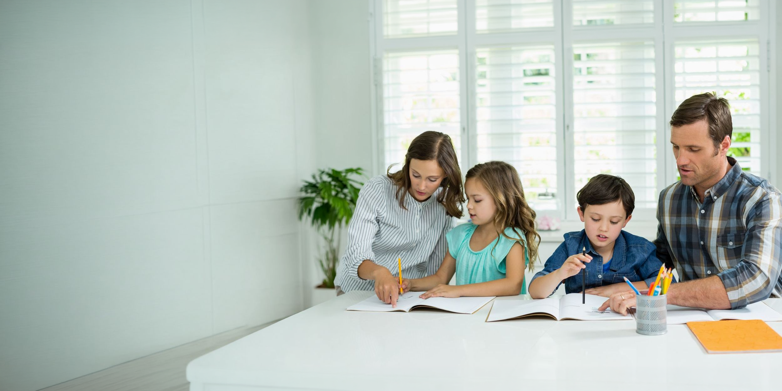 Mutter, Vater und zwei Kinder schreiben gemeinsam an einem hellen Tisch