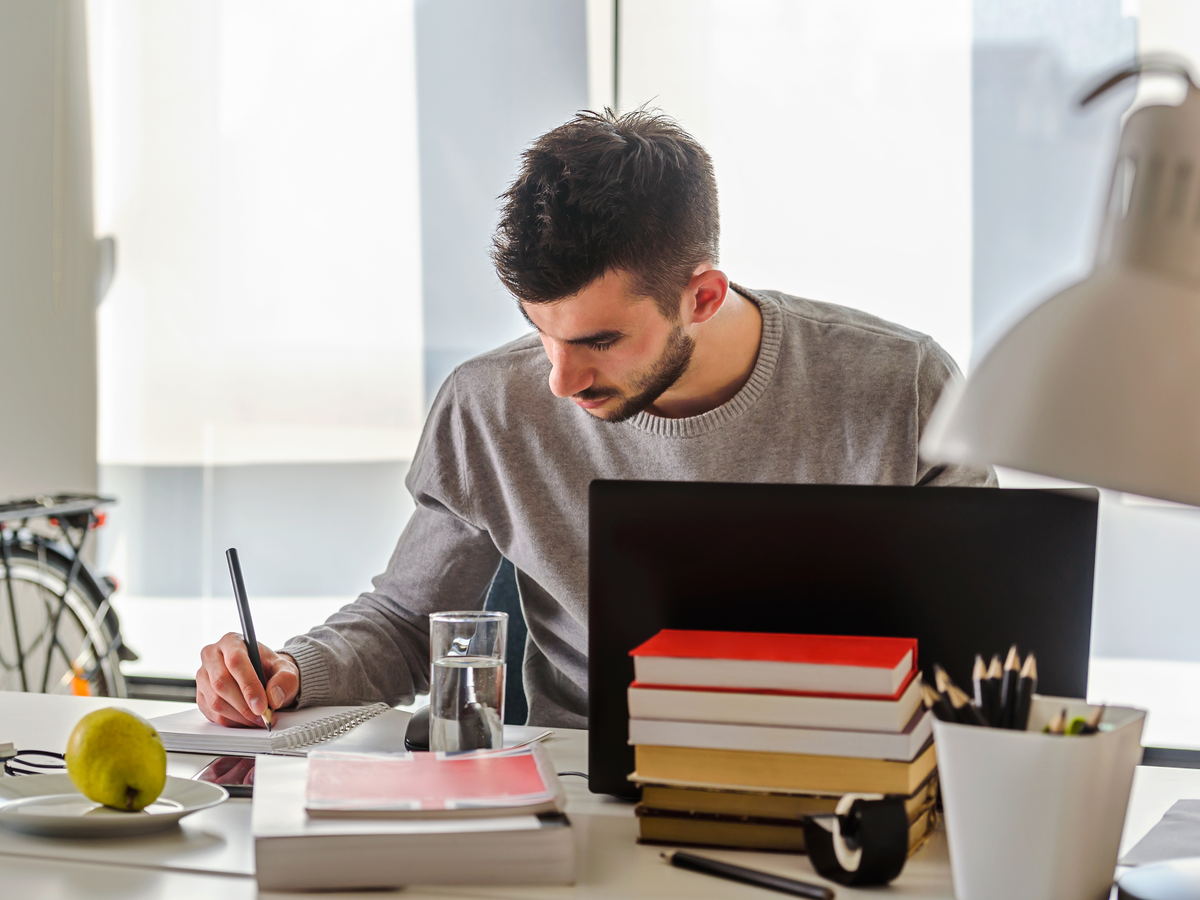 Junger Mann plant am Schreibtisch mit Büchern und Notizen