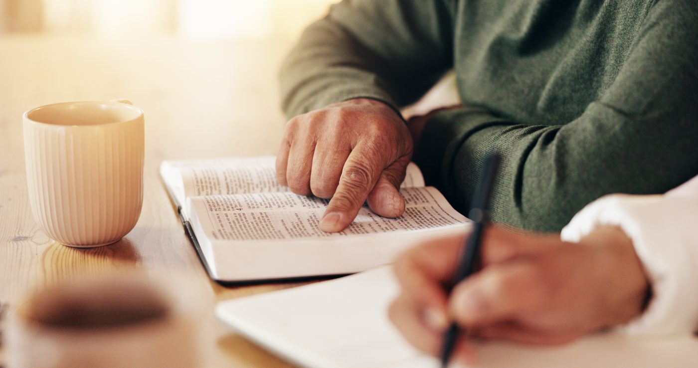 Aufgeschlagene Bibel, Notizbuch und schreibende Hände