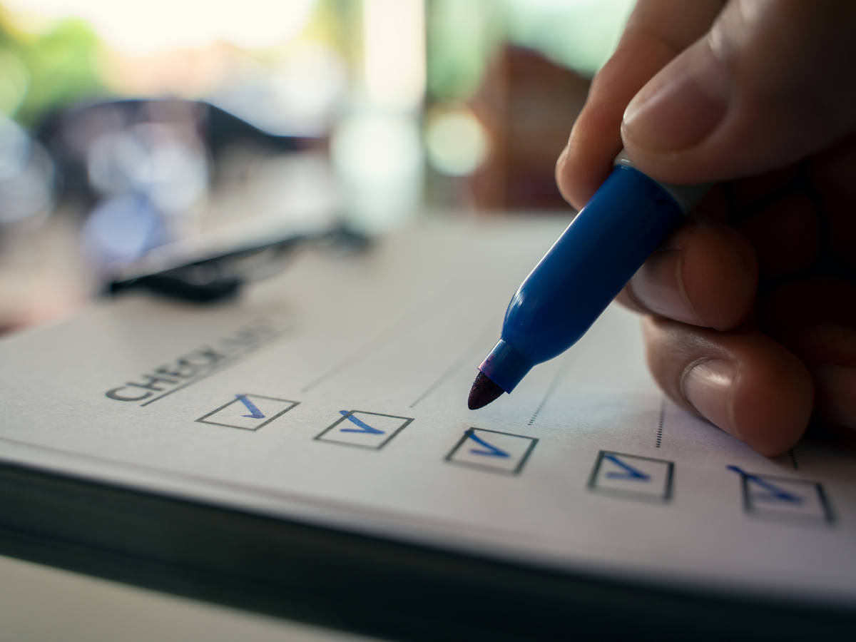 Hand setzt mit einem Stift Haken in eine Checkliste